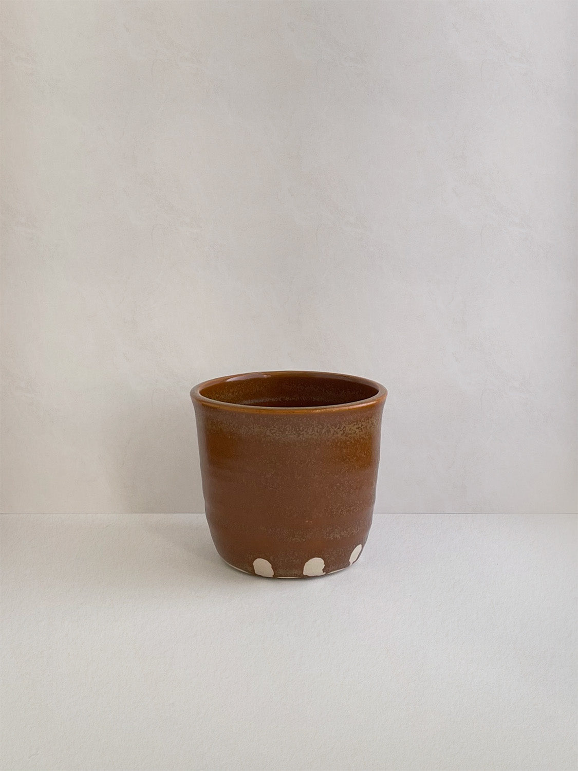 Burnt orange ceramic cup on a neutral background - back view.