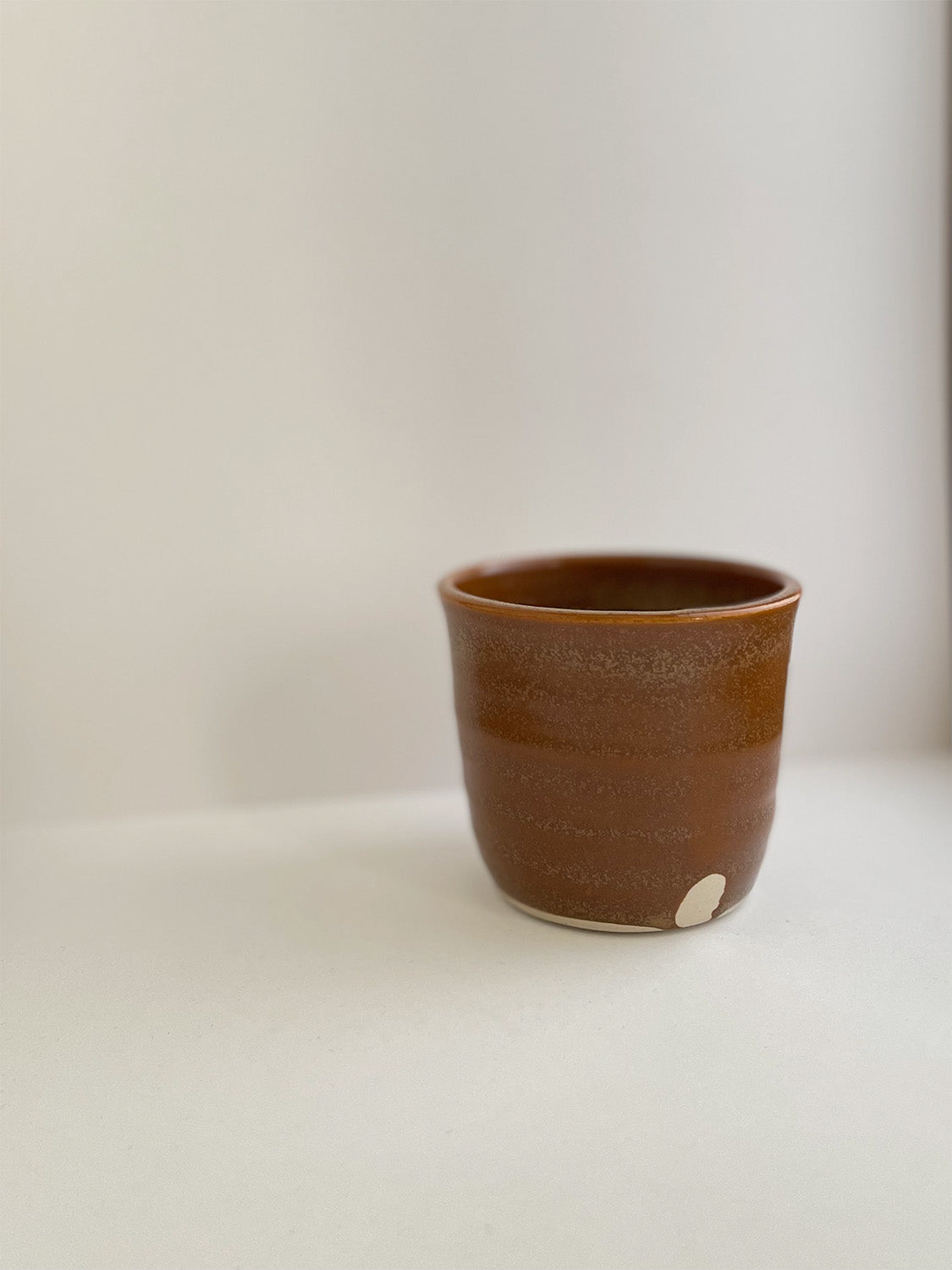 Burnt orange ceramic cup on a neutral background - detail view.