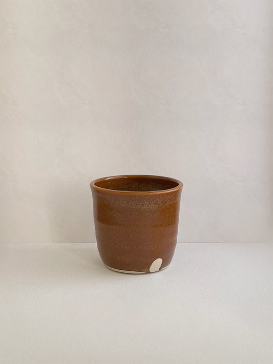 Burnt orange ceramic cup on a neutral background - front view.