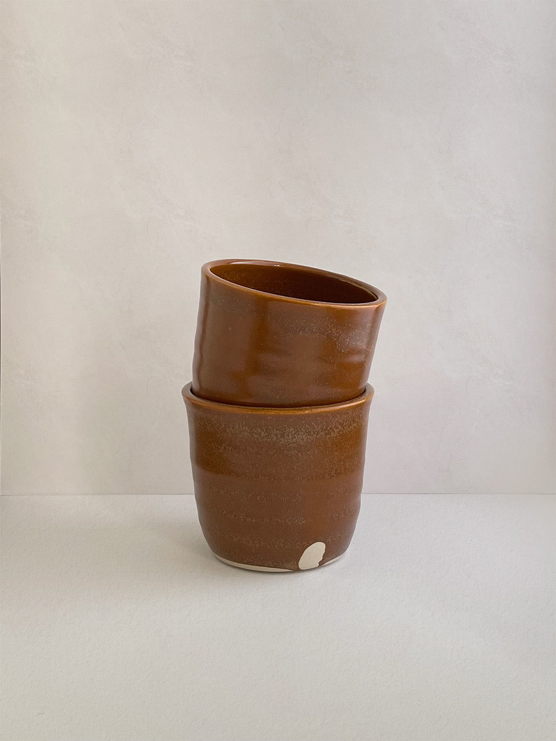 Two burnt orange ceramic cups stacked on a neutral background.