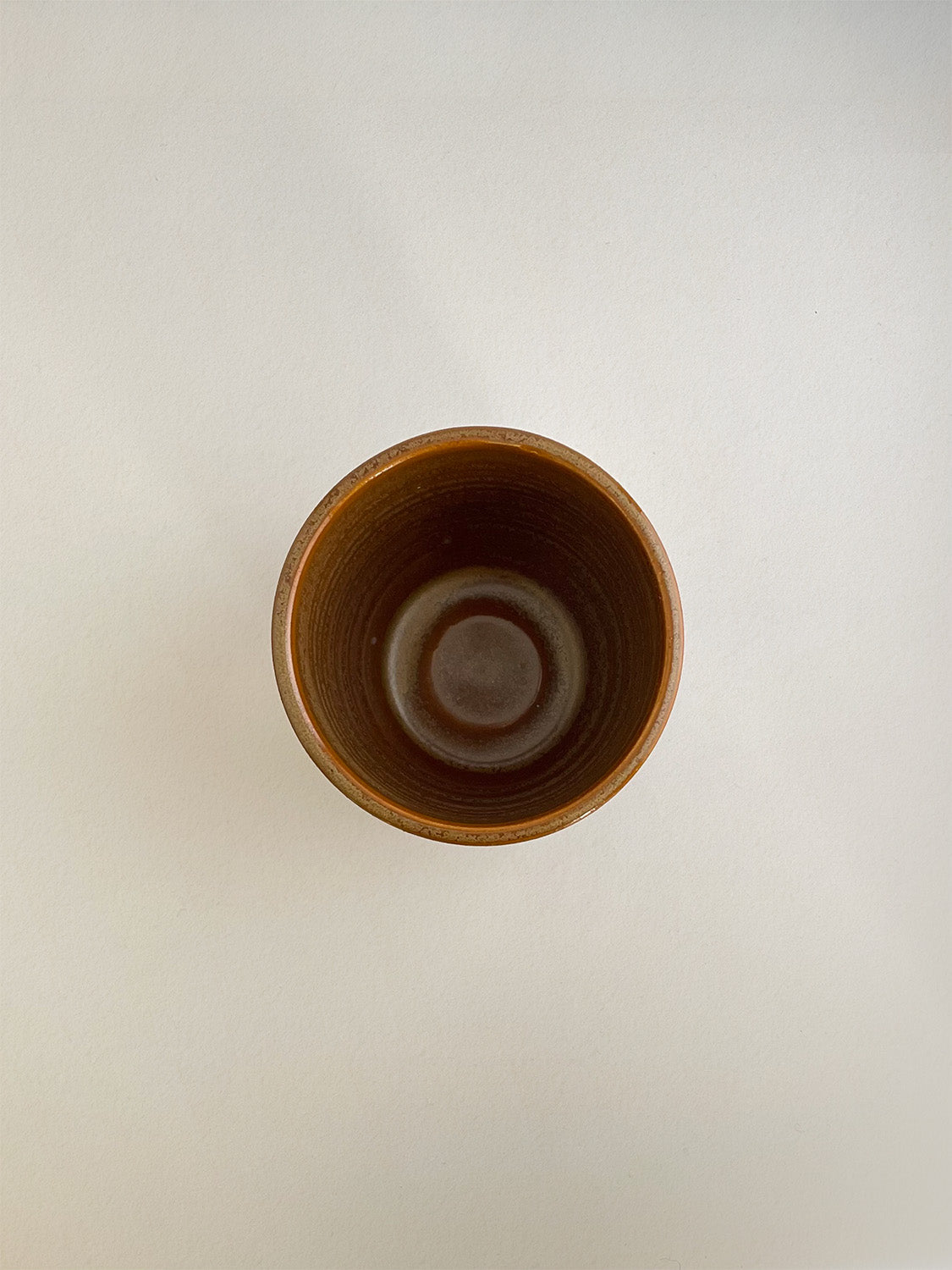 Burnt orange ceramic cup on a neutral background - top view.