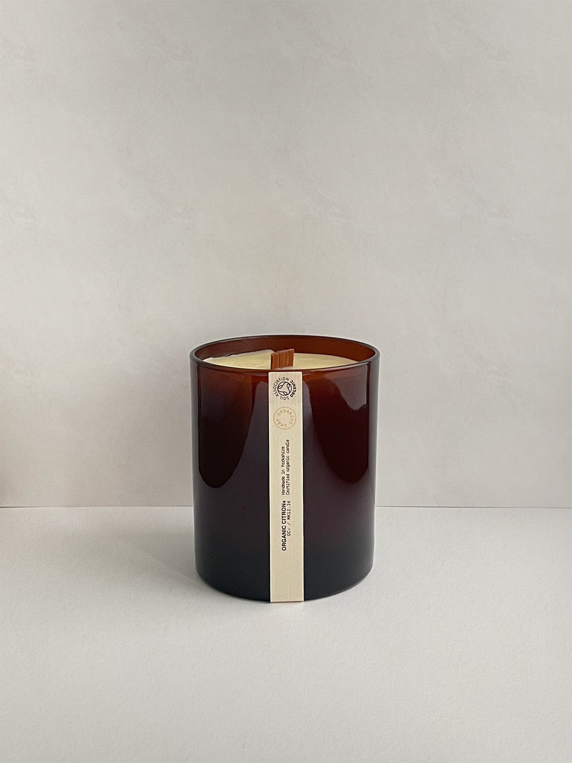 Candle in amber jar with a label on a light grey background.