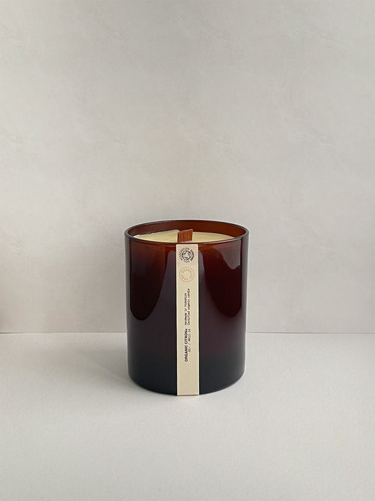 Candle in amber jar with a label on a light grey background.