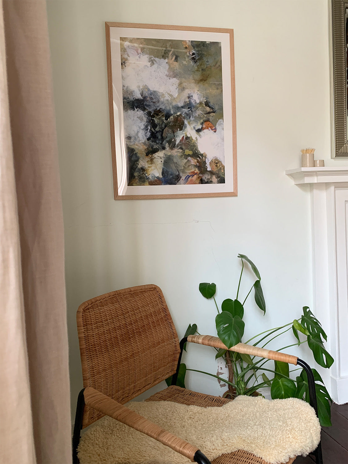 Wicker chair with a textured cushion in front of a wall with abstract art print and a plant.