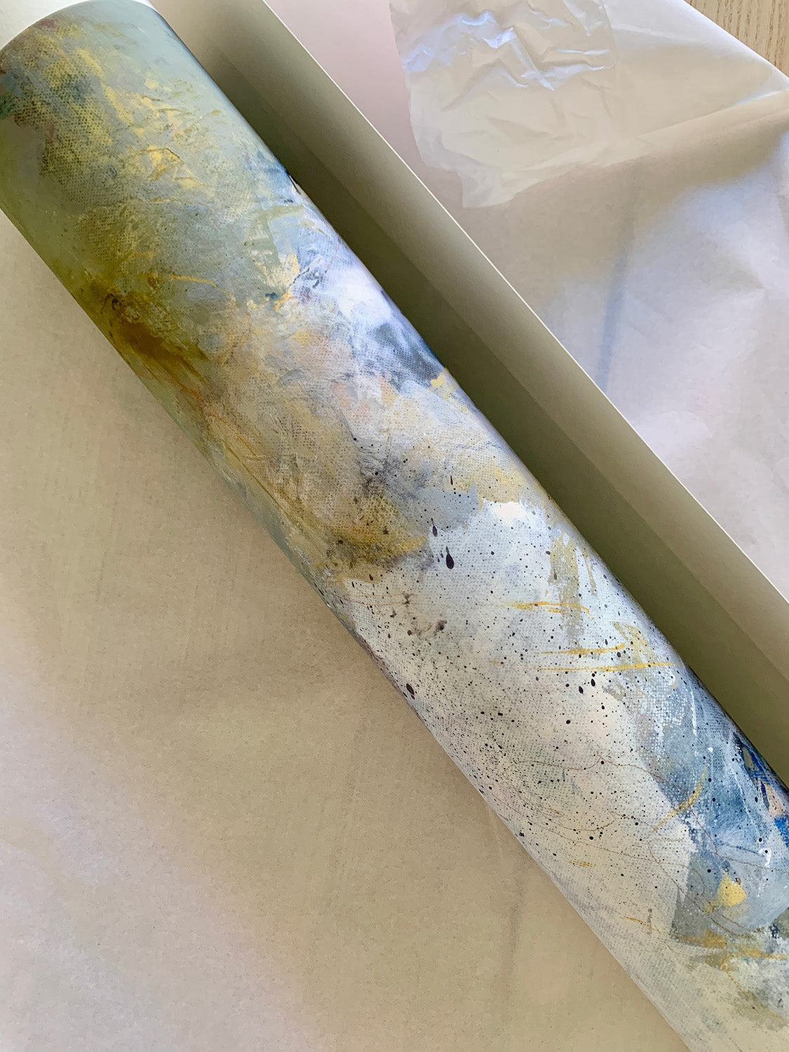 Close-up of rolled abstract art print with a mix of white, blue and gold colours.