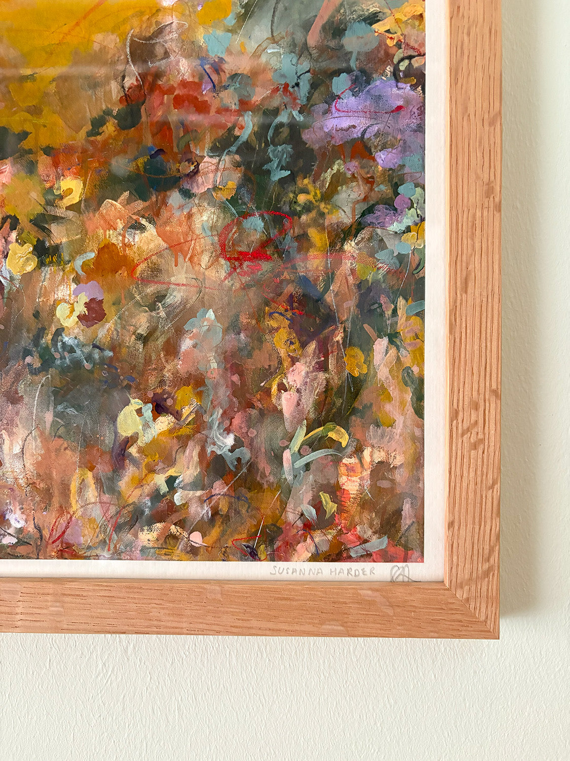 Close-up of abstract art print with warm, vibrant colours in a wooden frame on a white wall.