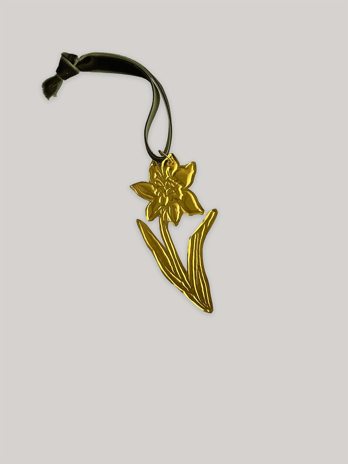 Gold tin daffodil handmade ornament with green velvet ribbon on a neutral background - back.