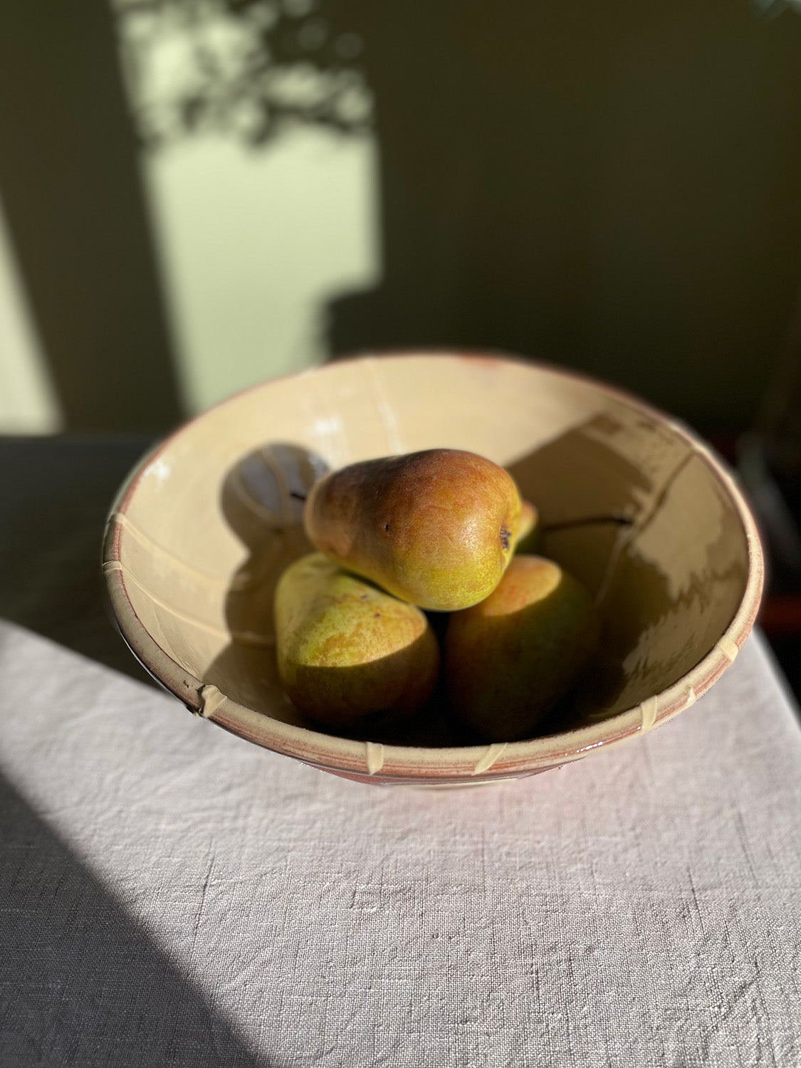 Ceramic serving bowl with pears on a linen tablecloth with a blurred background.