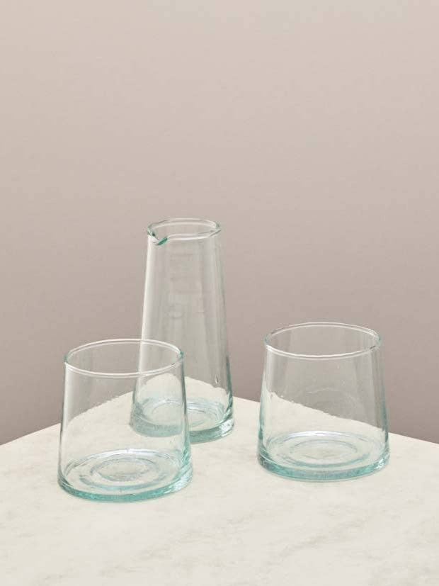Two clear glasses and a small jug on a light surface against a beige background.