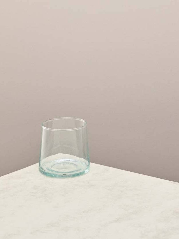 Clear glass low tumbler on a light surface with a beige background.