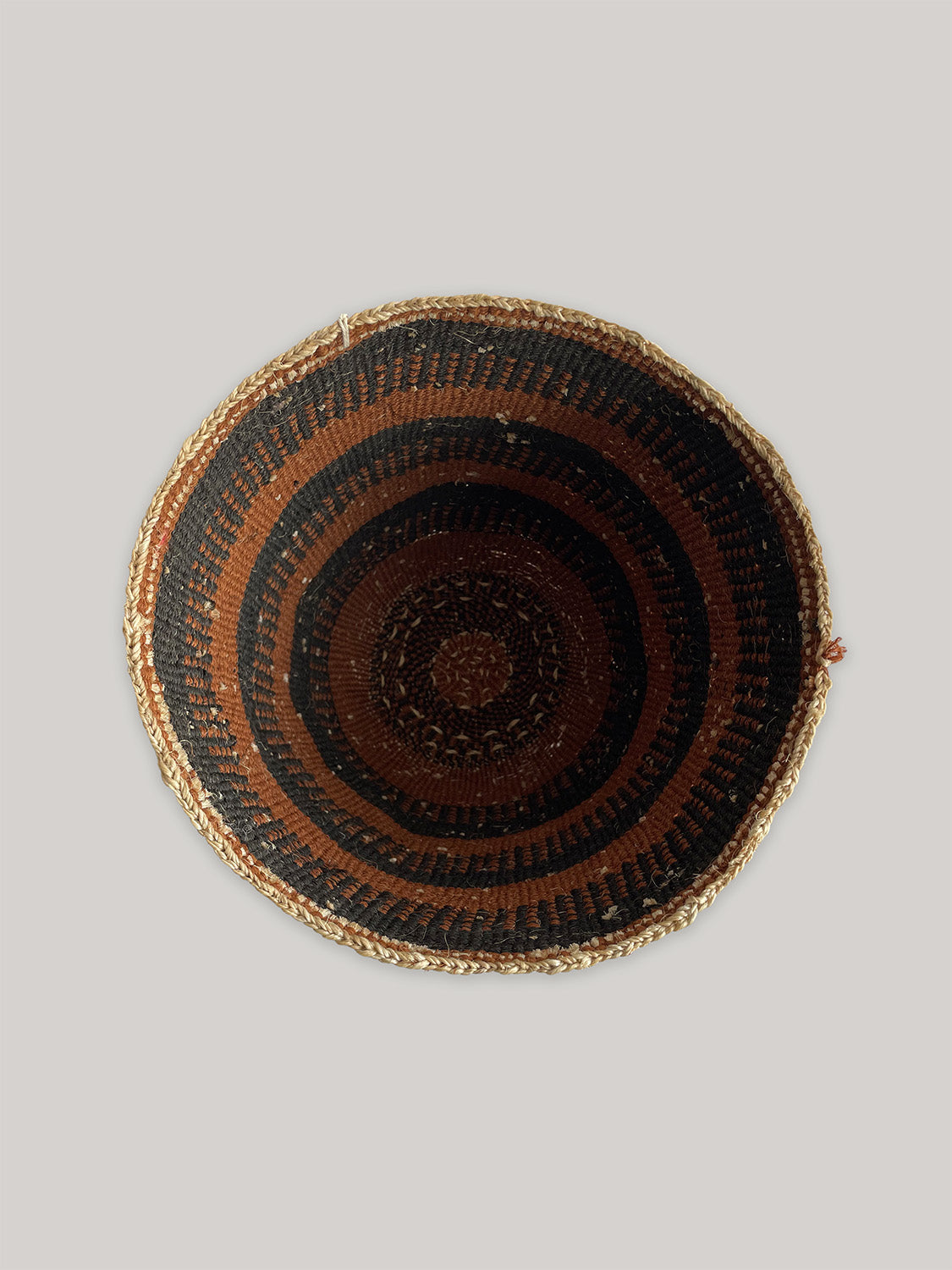 Woven basket with rust brown and black stripes on a neutral background - top view.