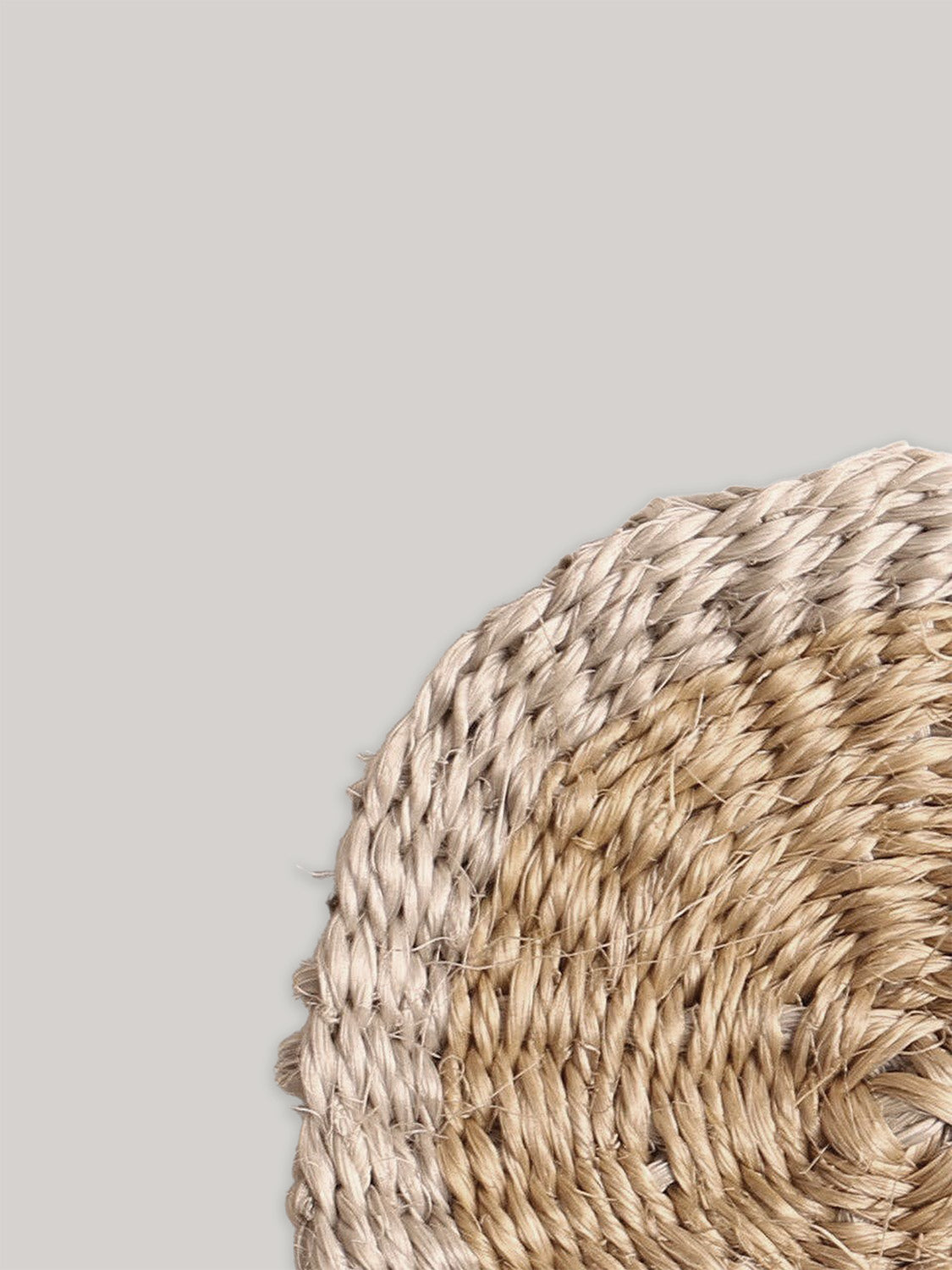 Close-up of round handwoven sisal coaster on a neutral background.