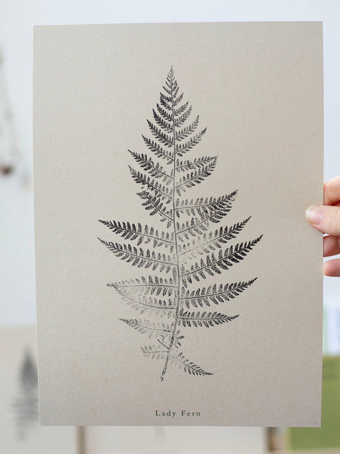 Print of a fern leaf on a beige background held by a hand.