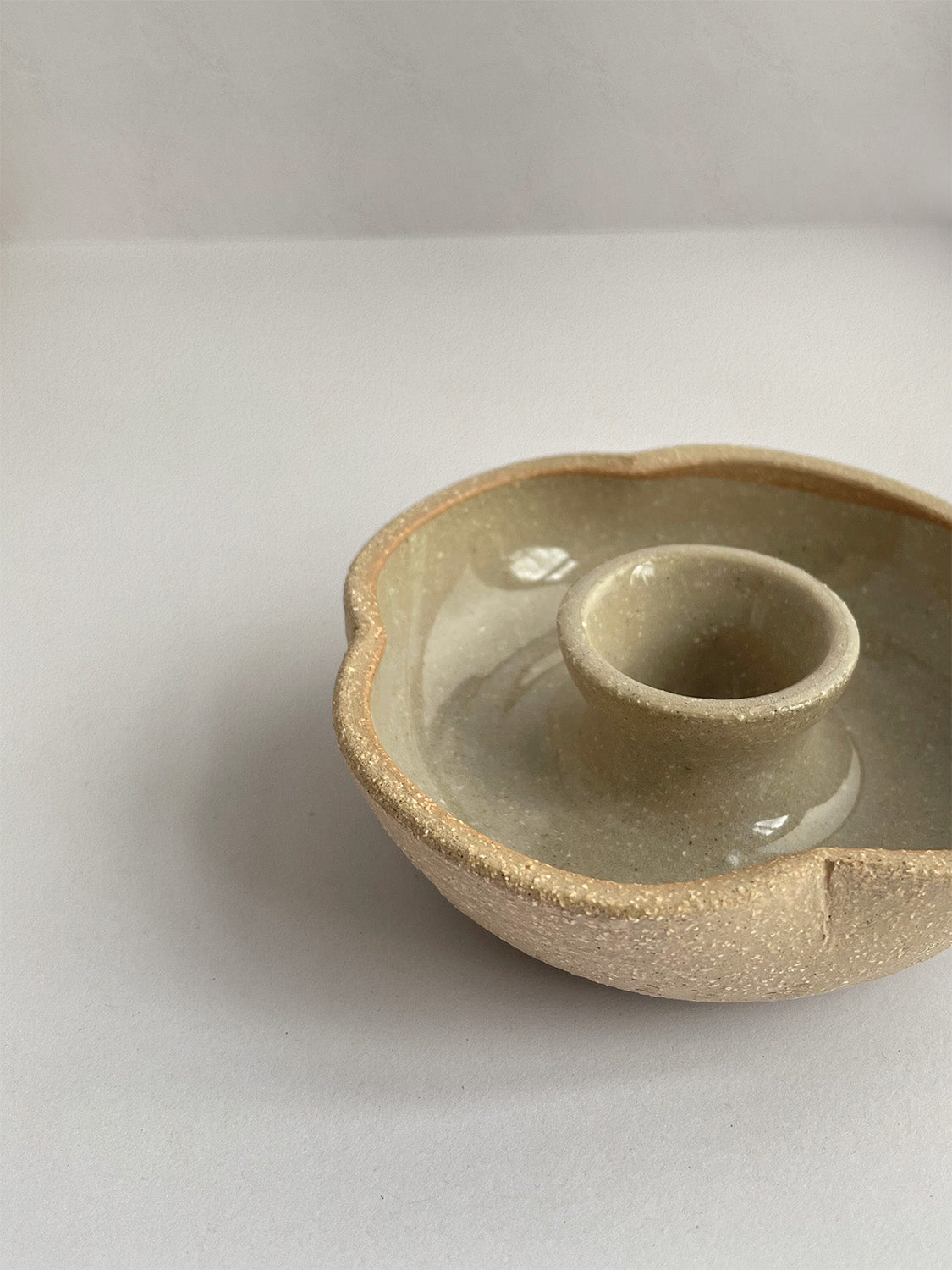 A hand-thrown ceramic candle holder in a rustic natural glaze on a neutral background - front view close-up.