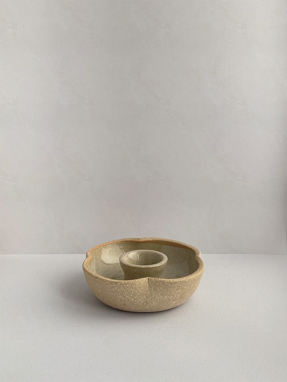 A hand-thrown ceramic candle holder in a rustic natural glaze on a neutral background - front view.