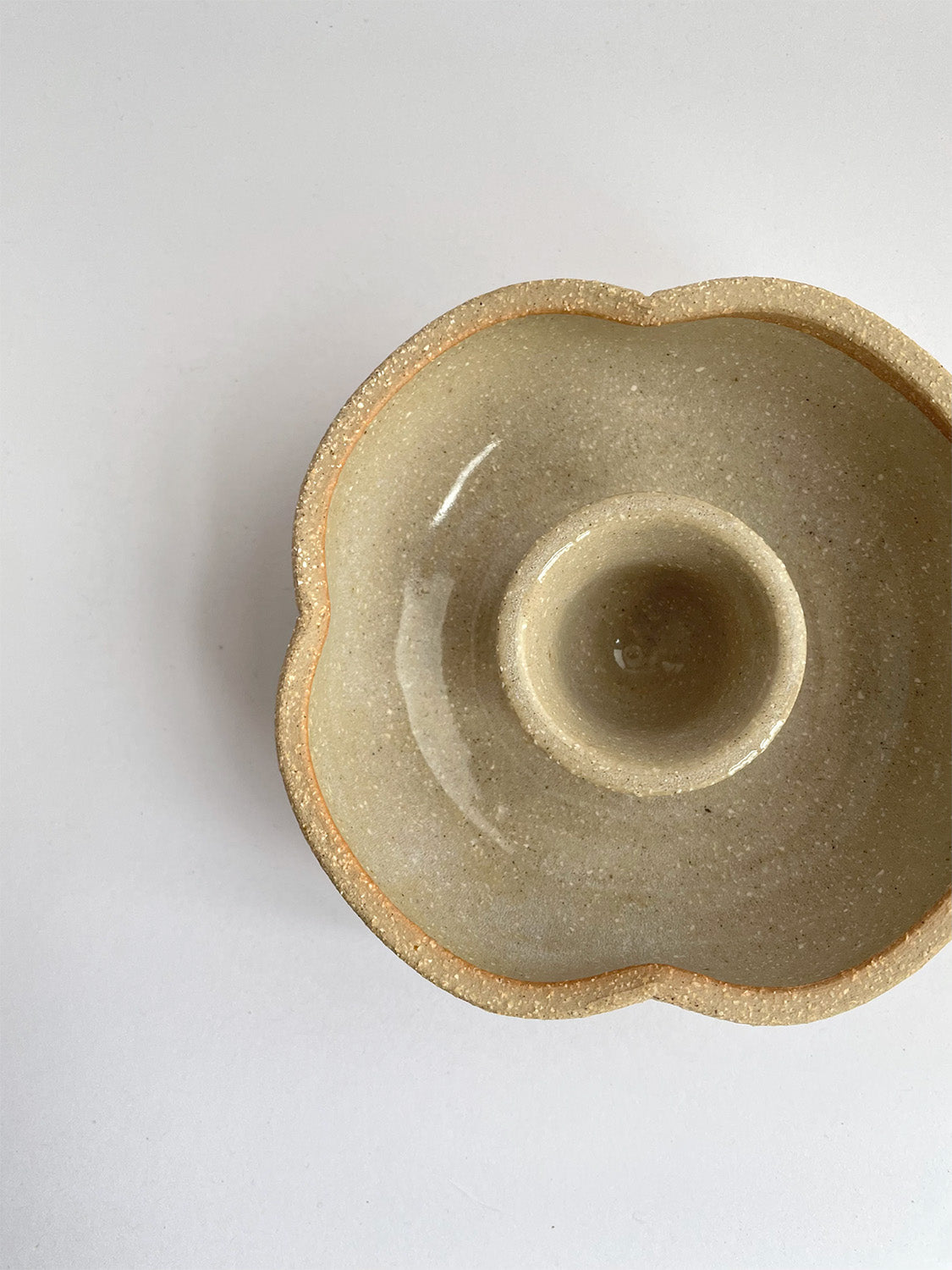 A hand-thrown ceramic candle holder in a rustic natural glaze on a neutral background - top view close-up.