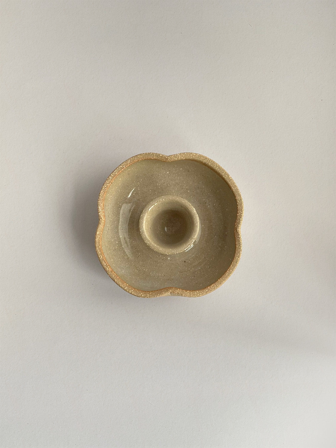 A hand-thrown ceramic candle holder in a rustic natural glaze on a neutral background - top view.