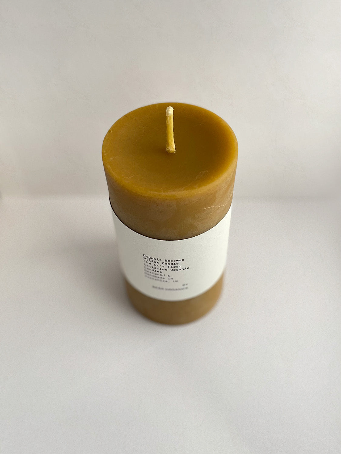 Organic beeswax pillar candle with label on a neutral background - front view 2.