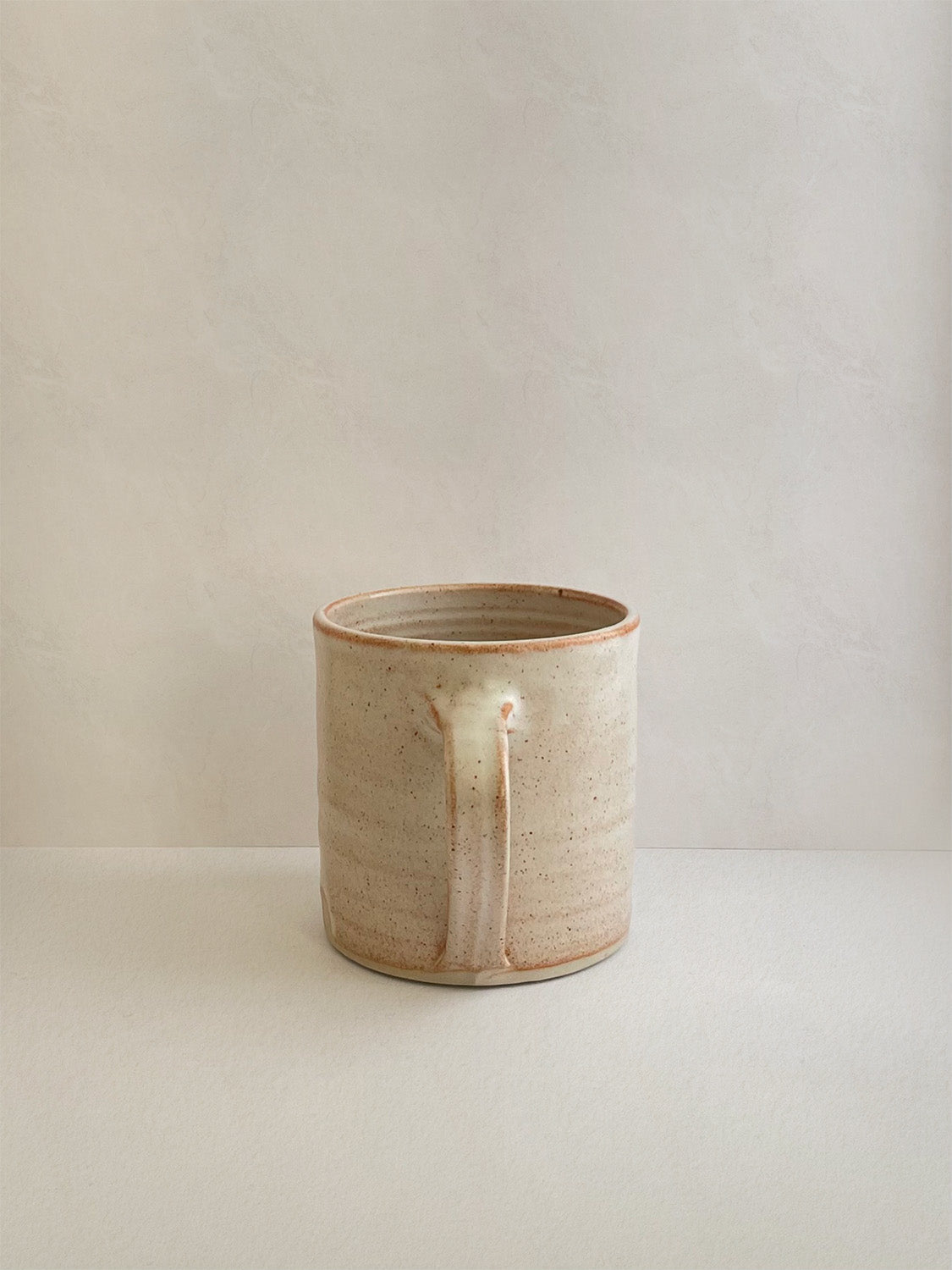 Rust ceramic mug on a neutral background - back view.