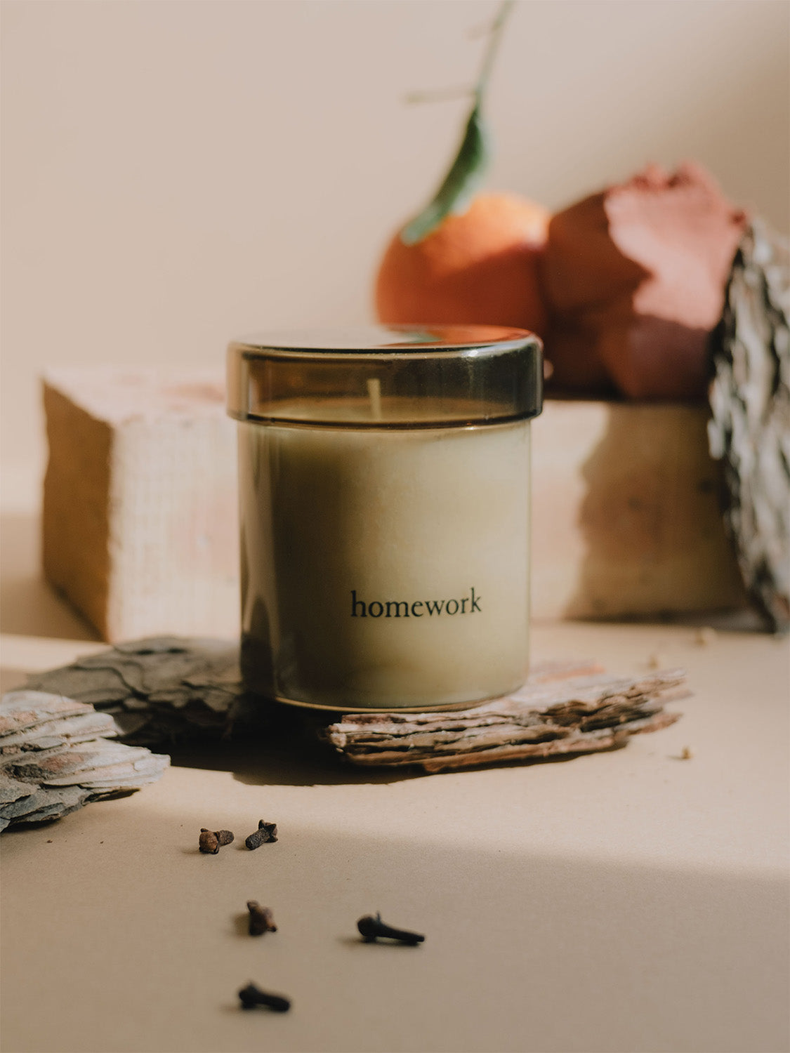 Candle in smoked glass jar labelled 'homework' on a surface with decorative elements.