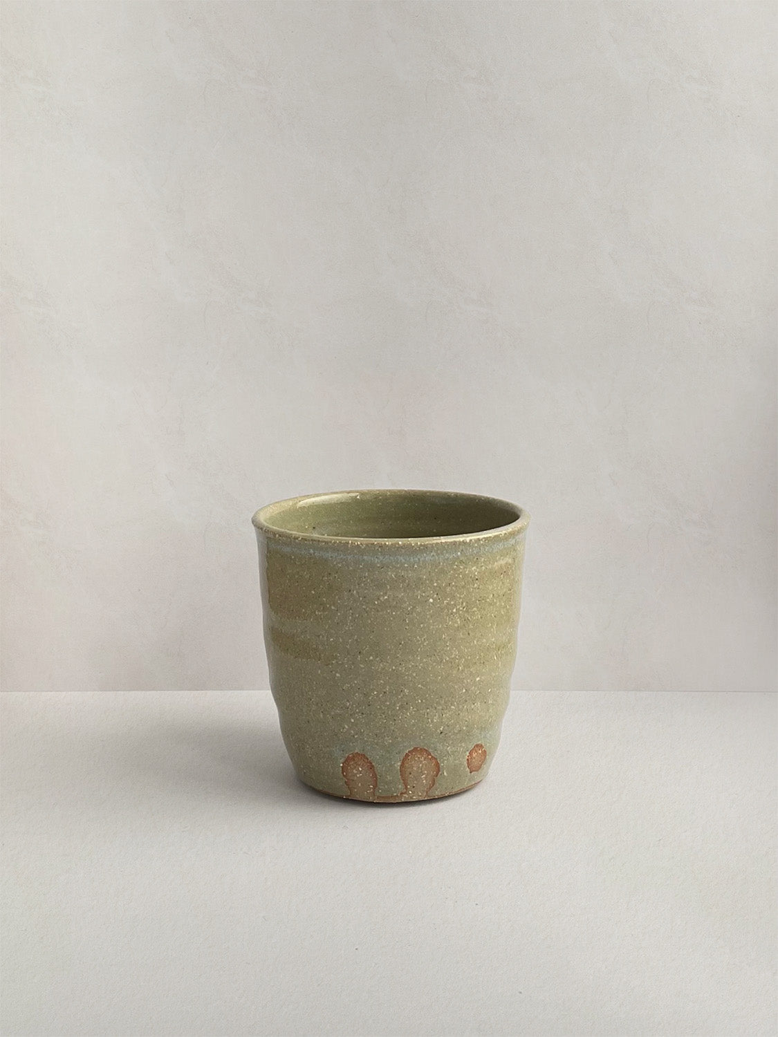 A handmade ceramic coffee cup with a rustic glaze finish, showing speckling and unique finger marks from the making process - back view.