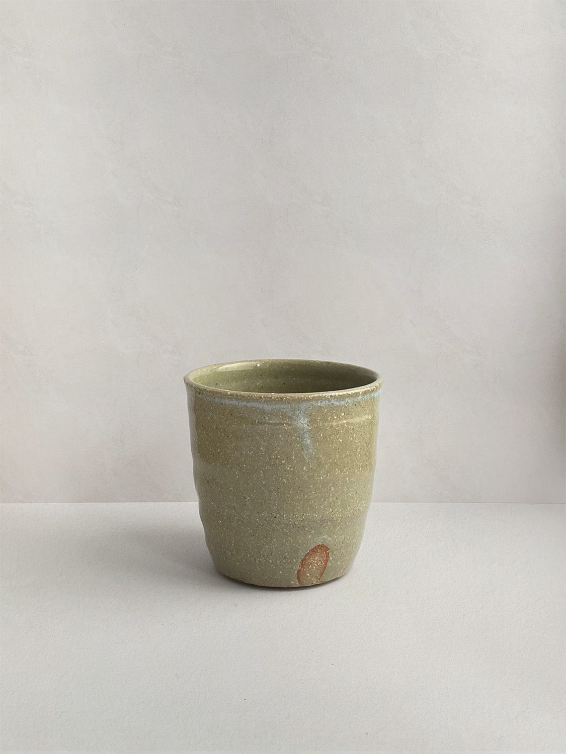 A handmade ceramic coffee cup with a rustic glaze finish, showing speckling and unique finger marks from the making process - front view.