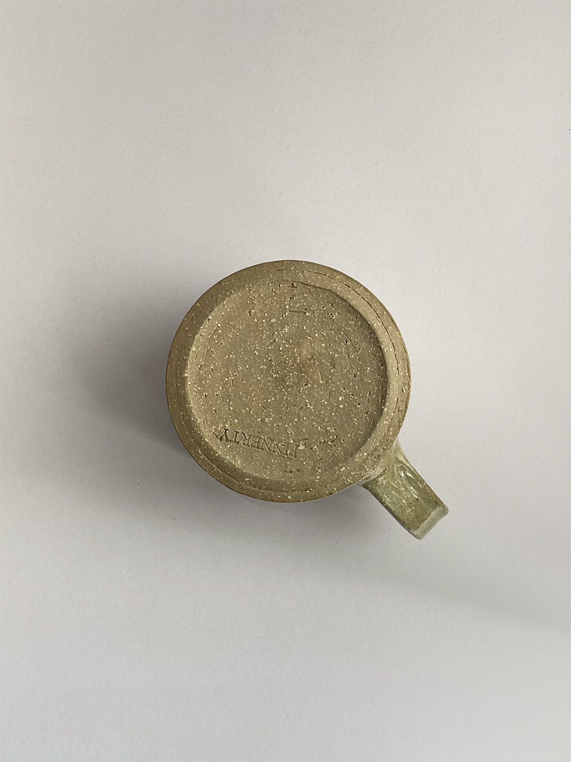 A rustic light green handmade ceramic espresso mug with a handle, on a neutral background - base view.