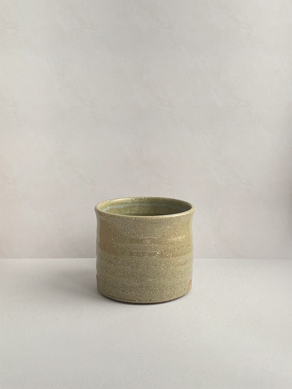 A rustic light green handmade ceramic espresso mug with a handle, on a neutral background - front view.