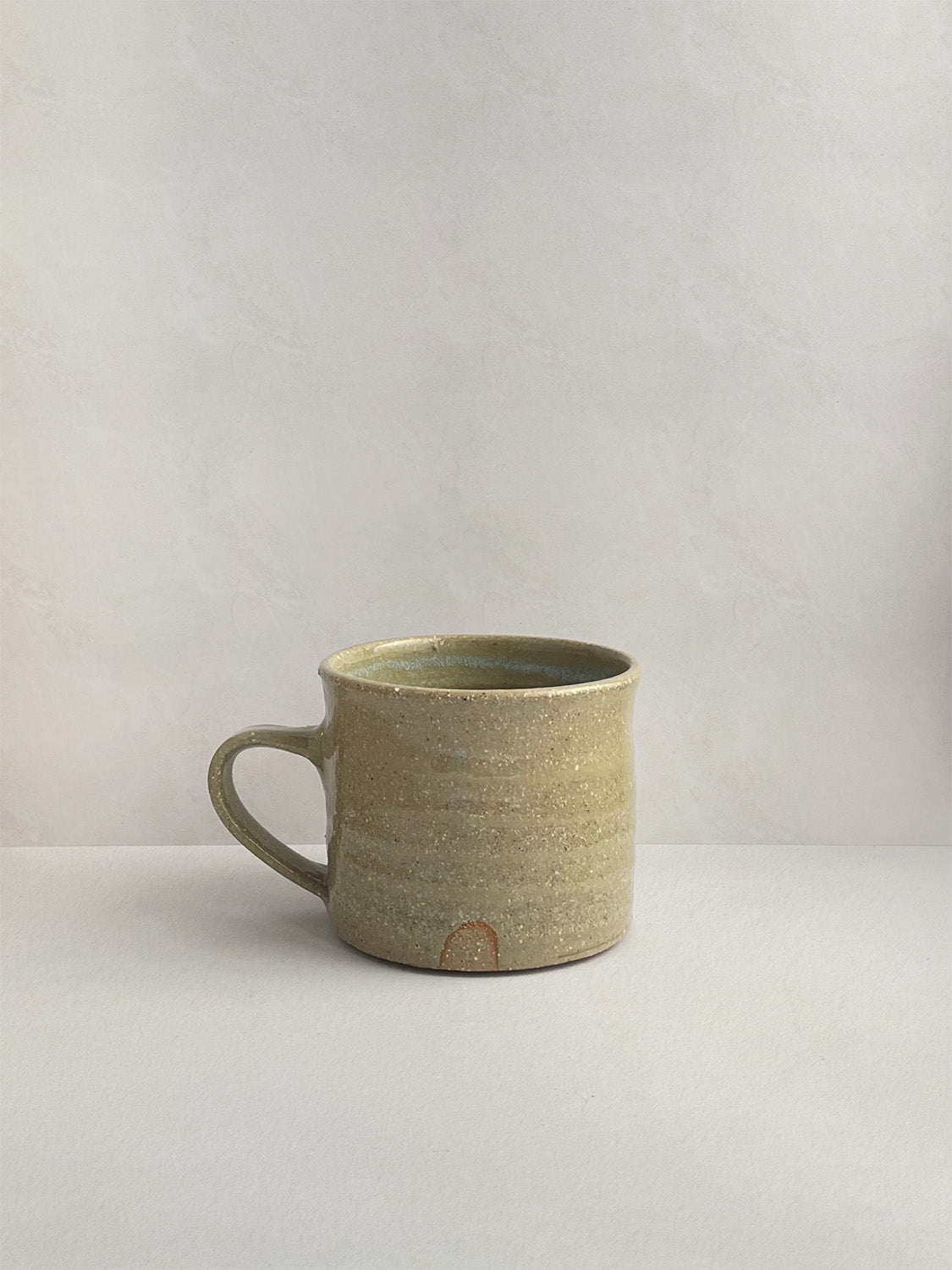 A rustic light green handmade ceramic espresso mug with a handle, on a neutral background - right side view.