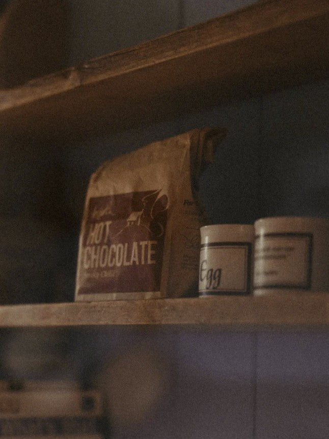 Hot chocolate mix and other items on a wooden shelf.