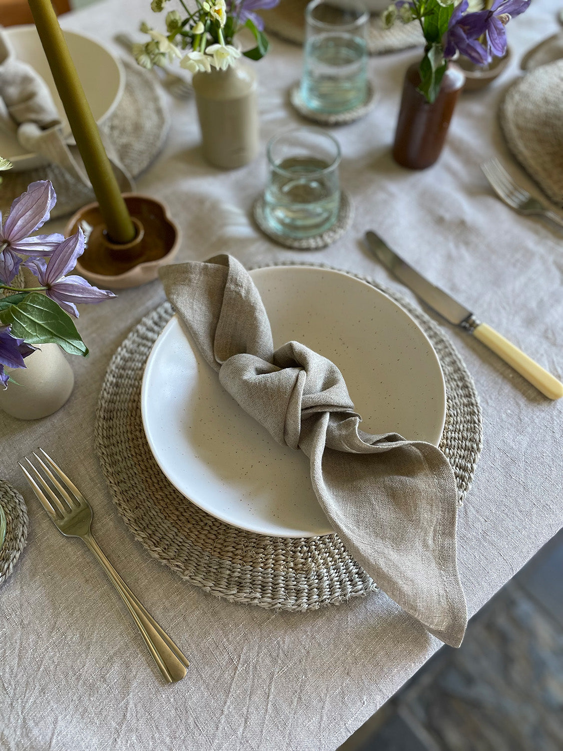 Elegant table setting with a white bowl, linen napkin, and decorative elements on a light-coloured tablecloth.