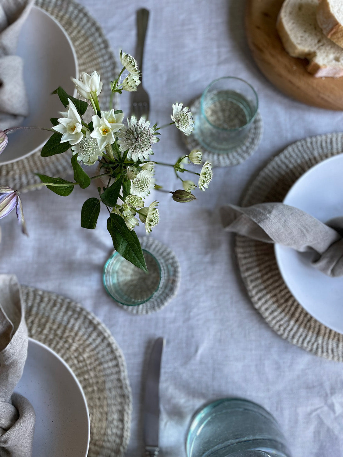 Elegant table setting with white flowers, bowls, and glasses on a light-coloured tablecloth.