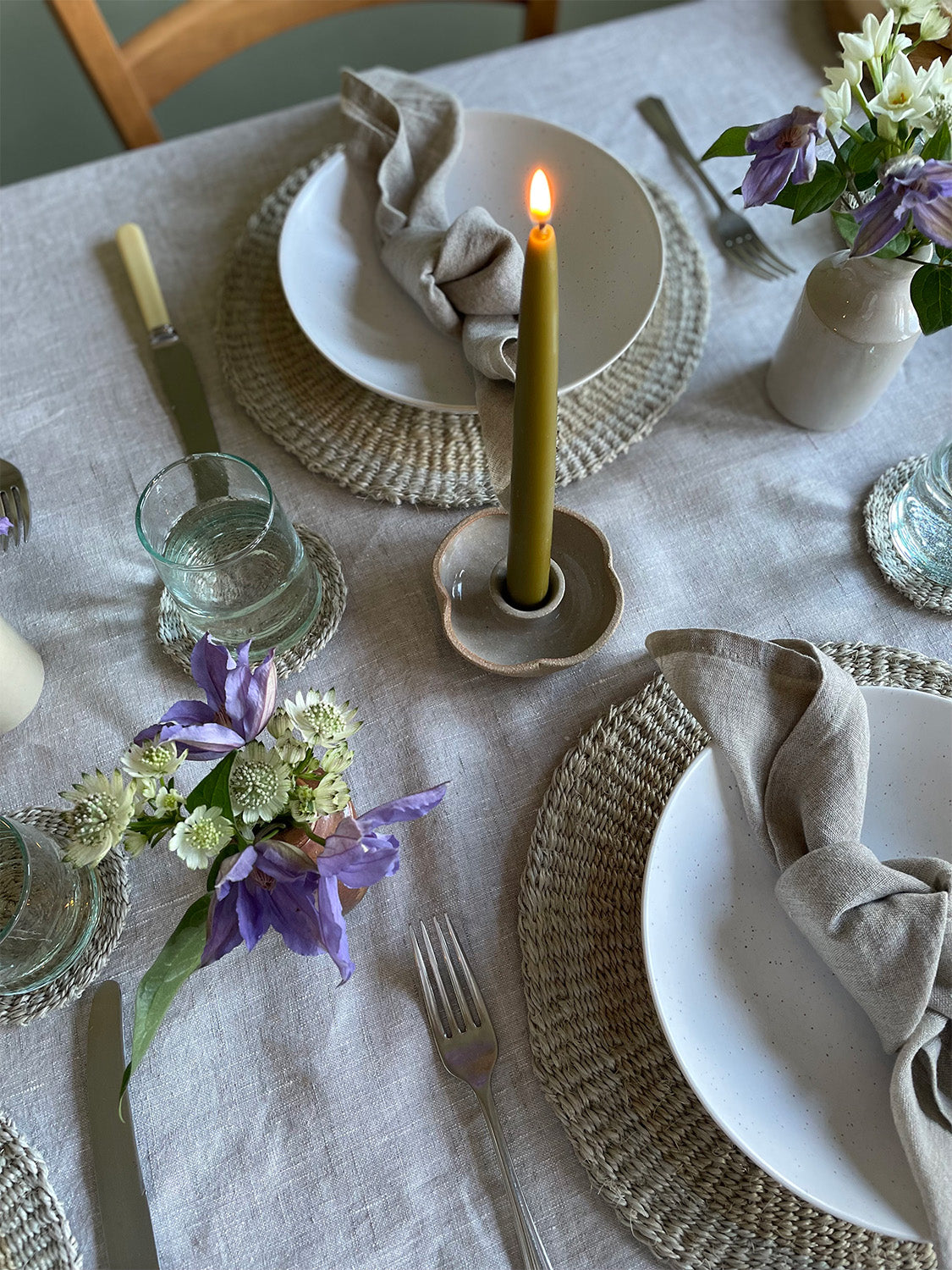 Elegant table setting with white bowls, woven placemats, flowers and a lit candle.
