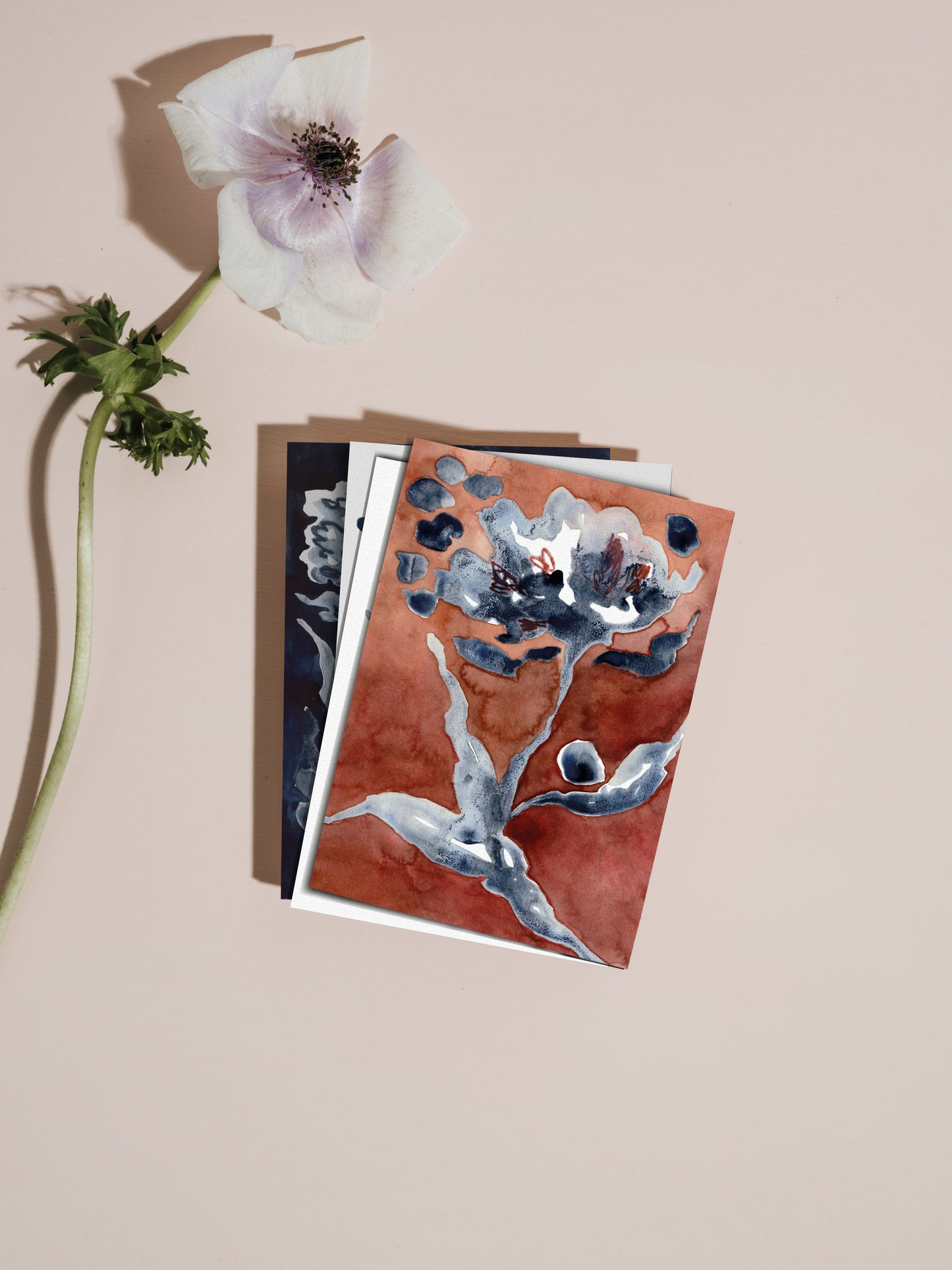 Stack of floral greetings cards with a white flower on a pale pink background.