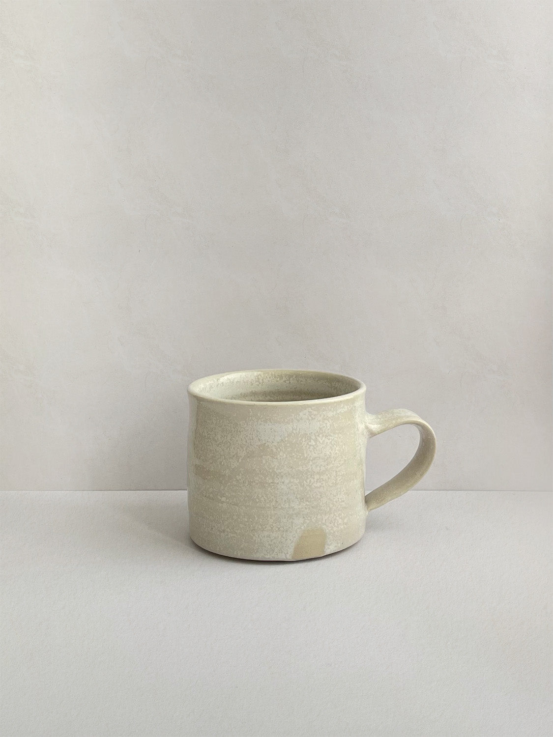 A beige handmade ceramic espresso mug with a handle, on a neutral background - left side view.