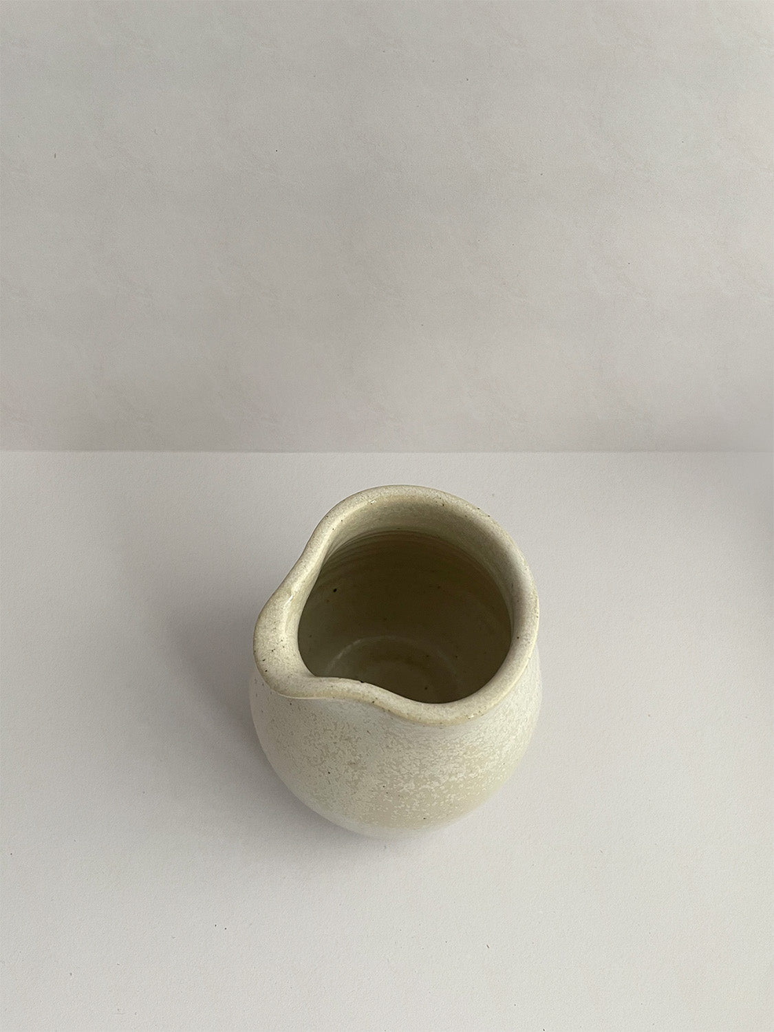 A hand-thrown ceramic milk jug in a beige speckled glaze on a neutral background - top view.