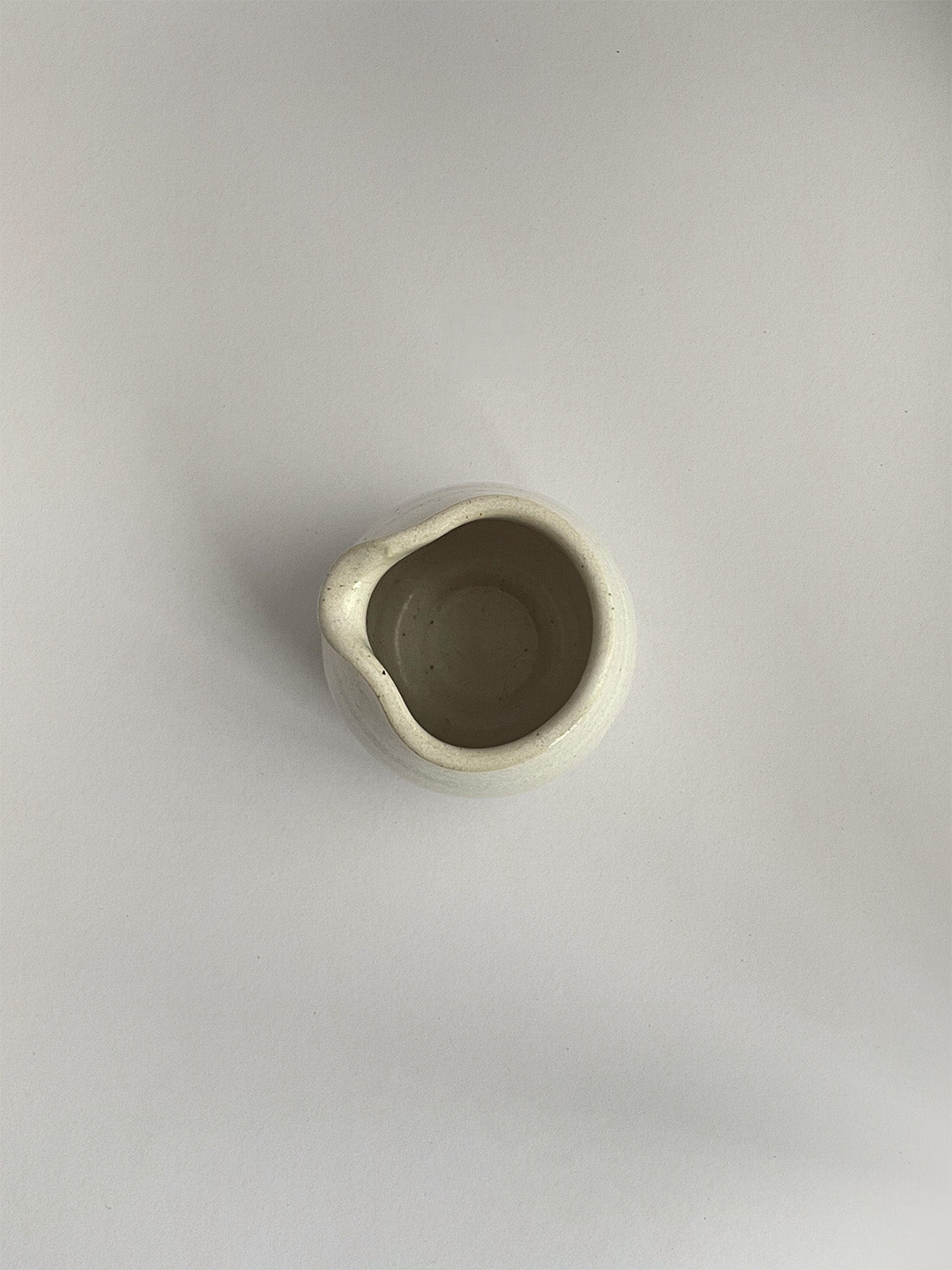 A hand-thrown ceramic milk jug in a beige speckled glaze on a neutral background - top view.