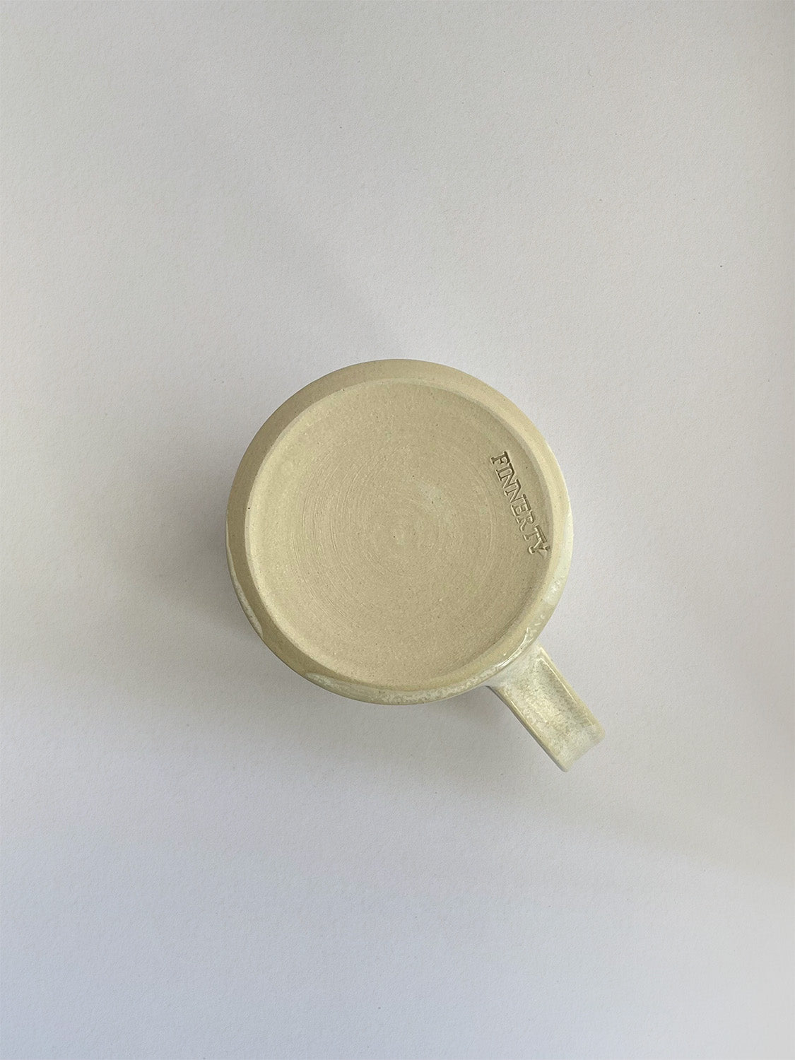 A hand-thrown ceramic mug with a handle, in a beige speckled glaze on a neutral background - base view.