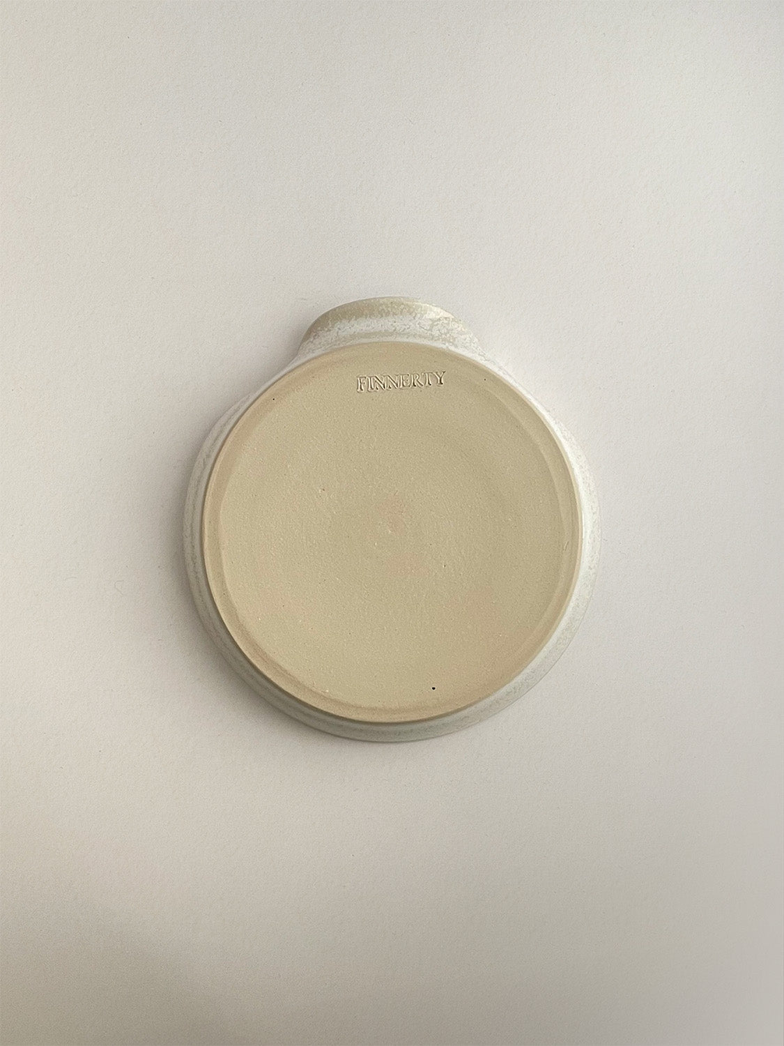Warm white mottled ceramic spoon rest on a neutral background - base view.