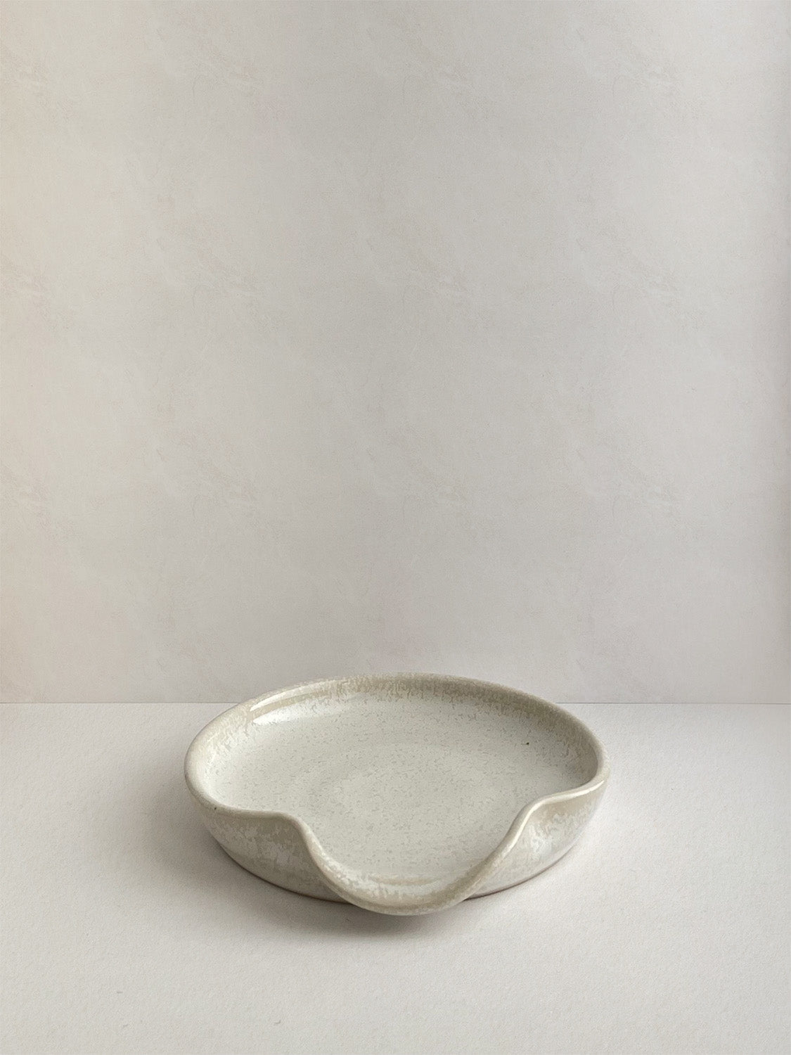 Warm white mottled ceramic spoon rest on a neutral background - front view.