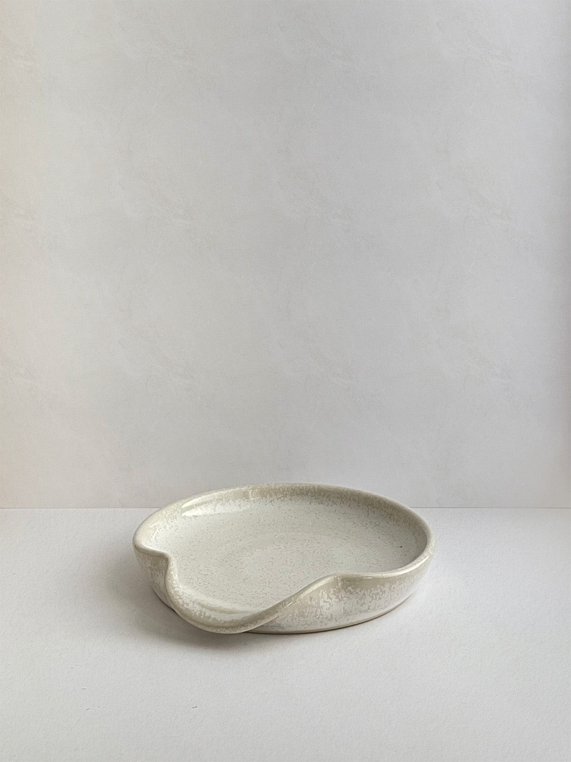 Warm white mottled ceramic spoon rest on a neutral background - front view.