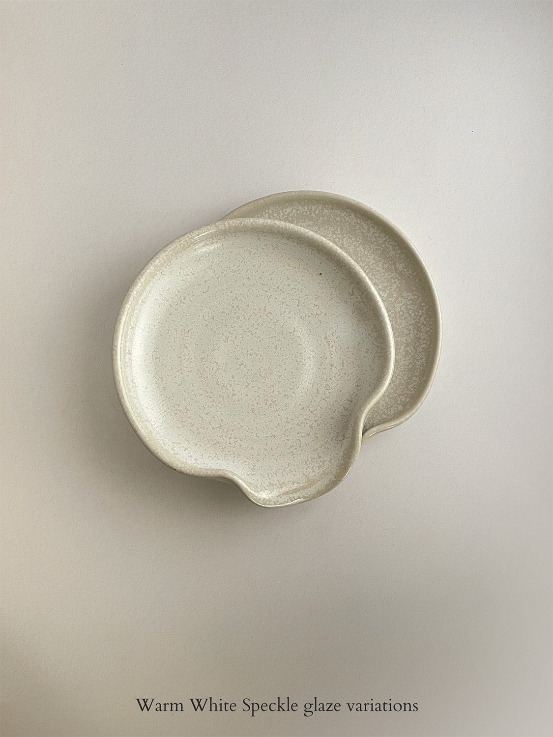 Pair of warm white mottled ceramic spoon rests on a neutral background.