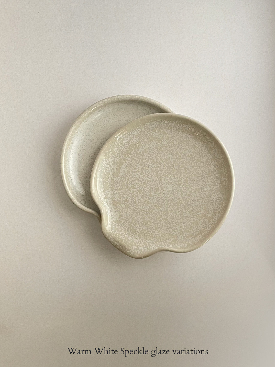 Pair of warm white mottled ceramic spoon rests on a neutral background.