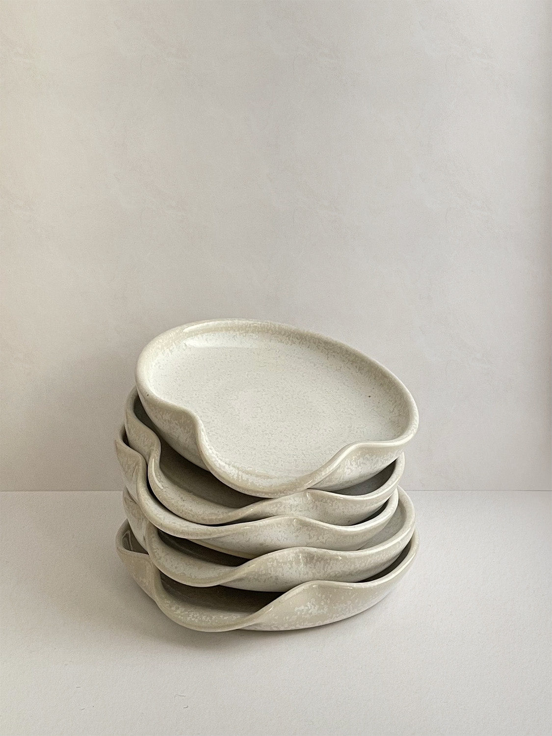 Stack of warm white mottled ceramic spoon rests on a neutral background.