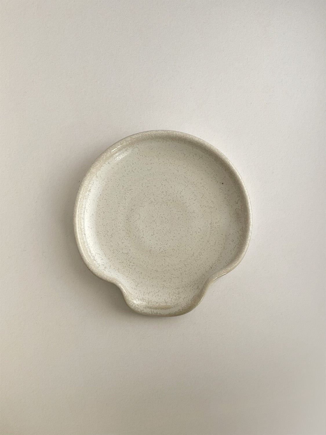 Warm white mottled ceramic spoon rest on a neutral background - top view.