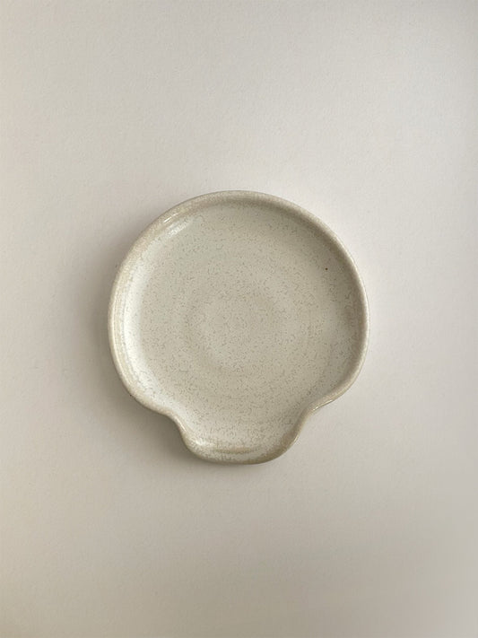 Warm white mottled handmade ceramic spoon rest on a neutral background - top view.