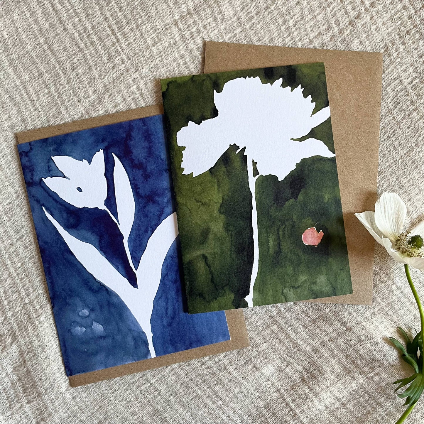 Two greeting cards with floral designs on a textured surface.