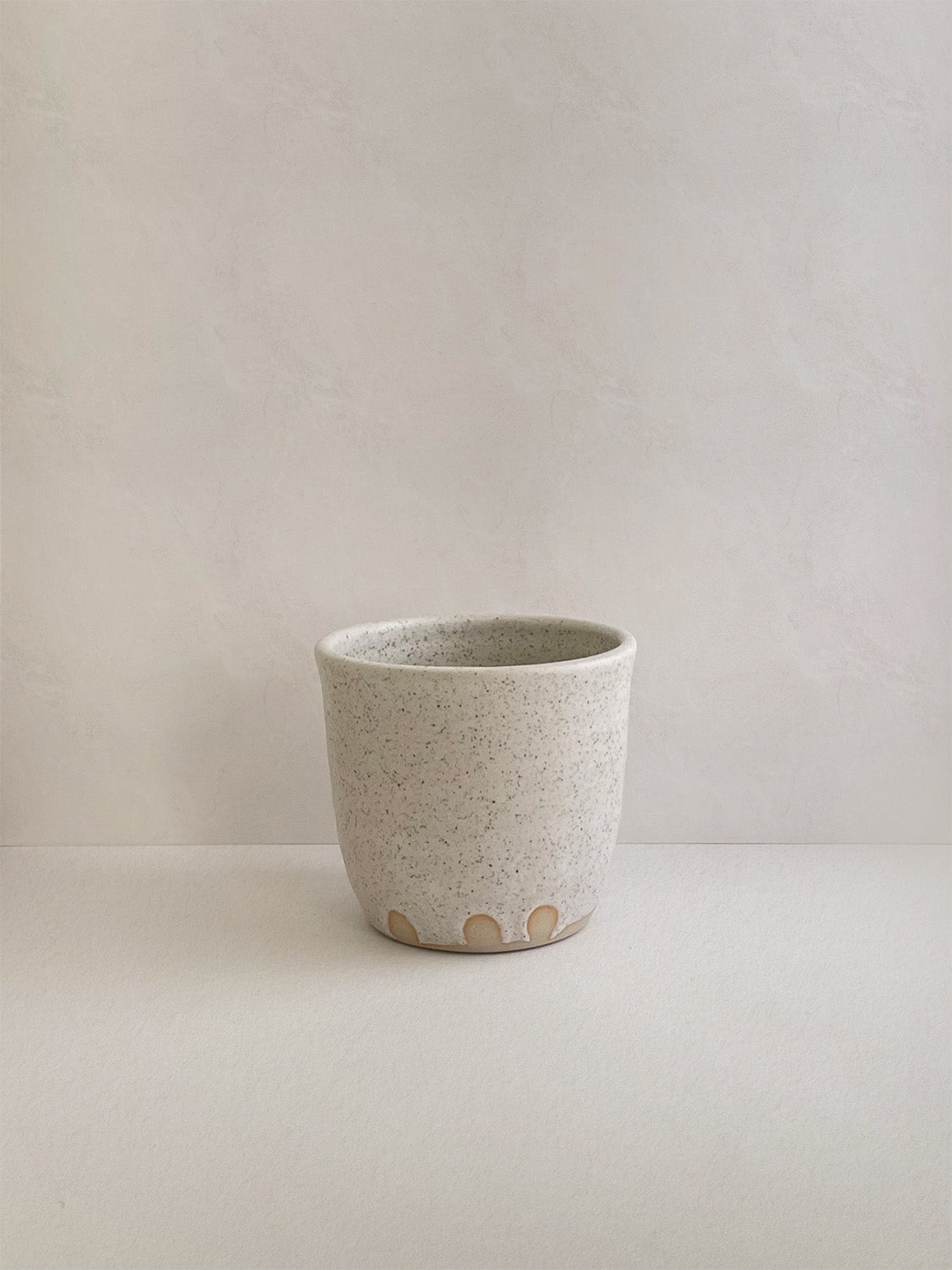 Speckled white ceramic cup on a neutral background - back view.