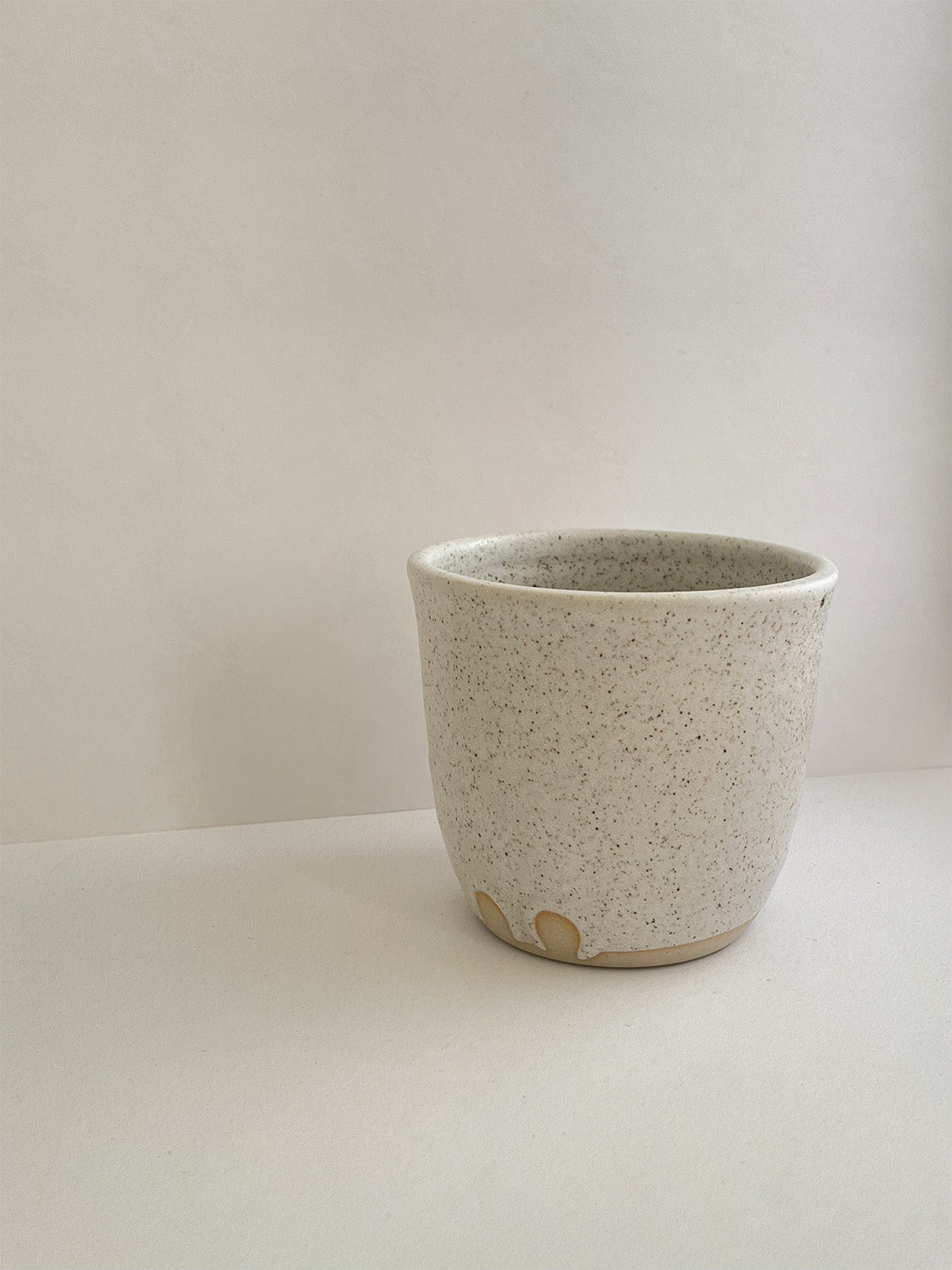 Speckled white ceramic cup on a neutral background - detail view.