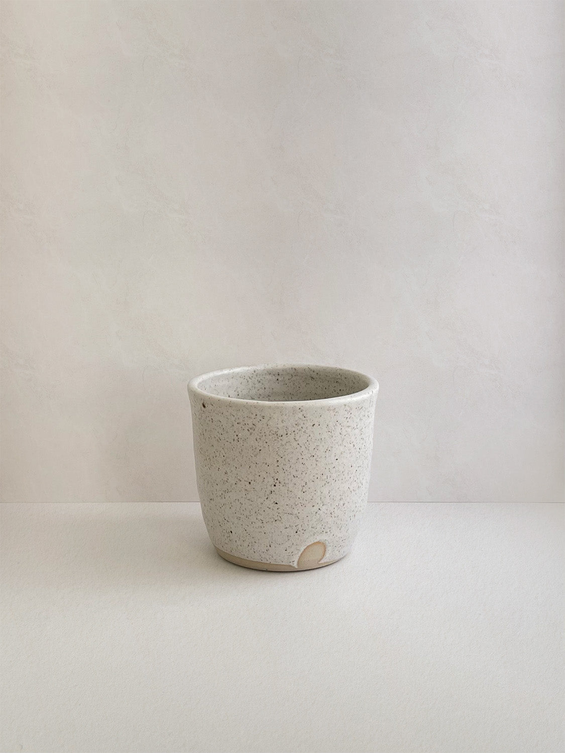 Speckled white ceramic cup on a neutral background - front view.
